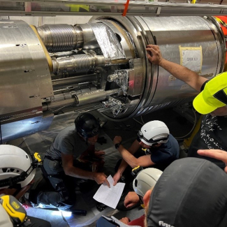 CERN technicians and engineers examine the faulty interconnection between triplet magnets (in orange)
